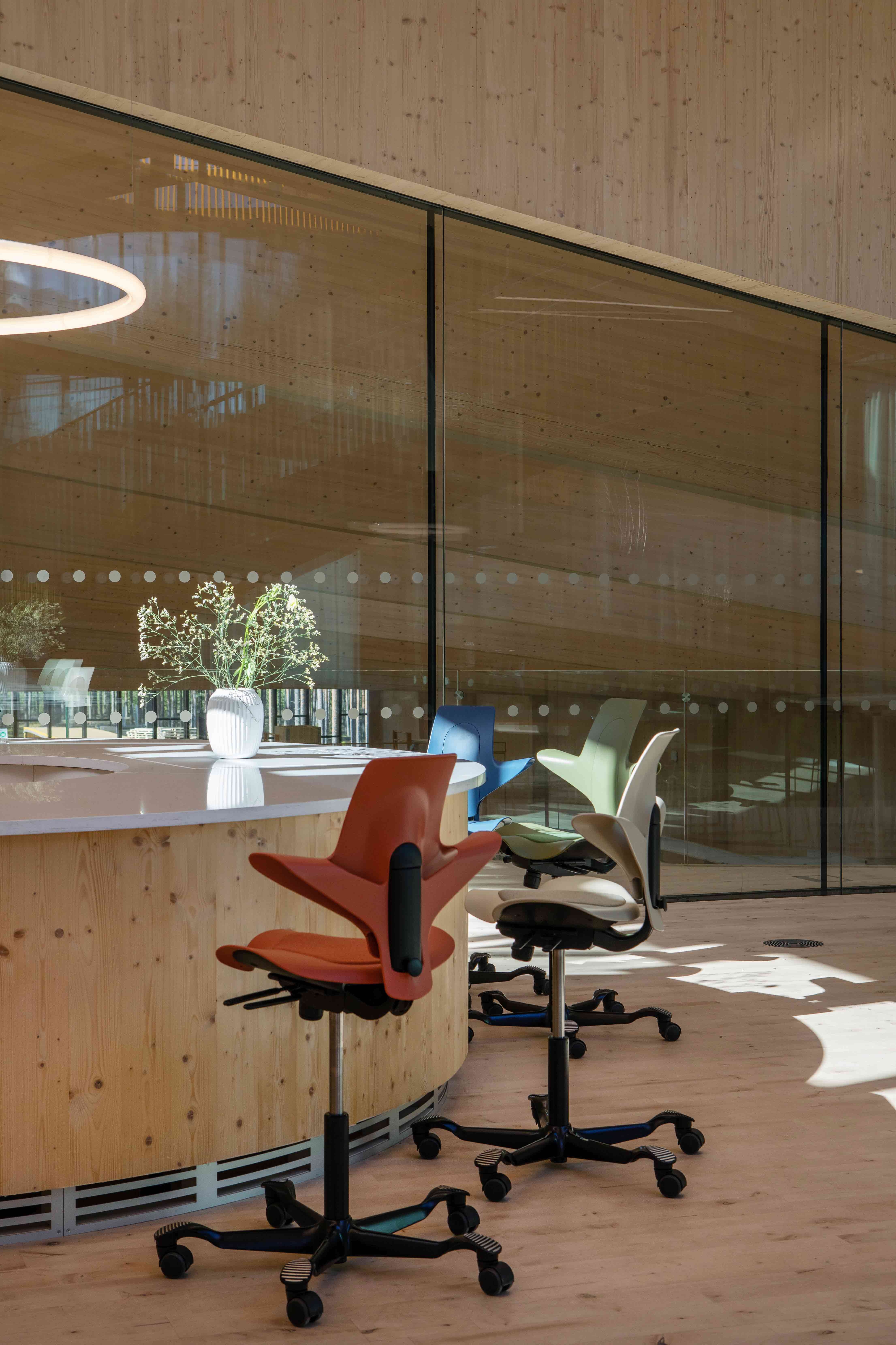 Kleurrijke ergonomische bureaustoelen bij ronde houten balie met witte vaas en bloemen.