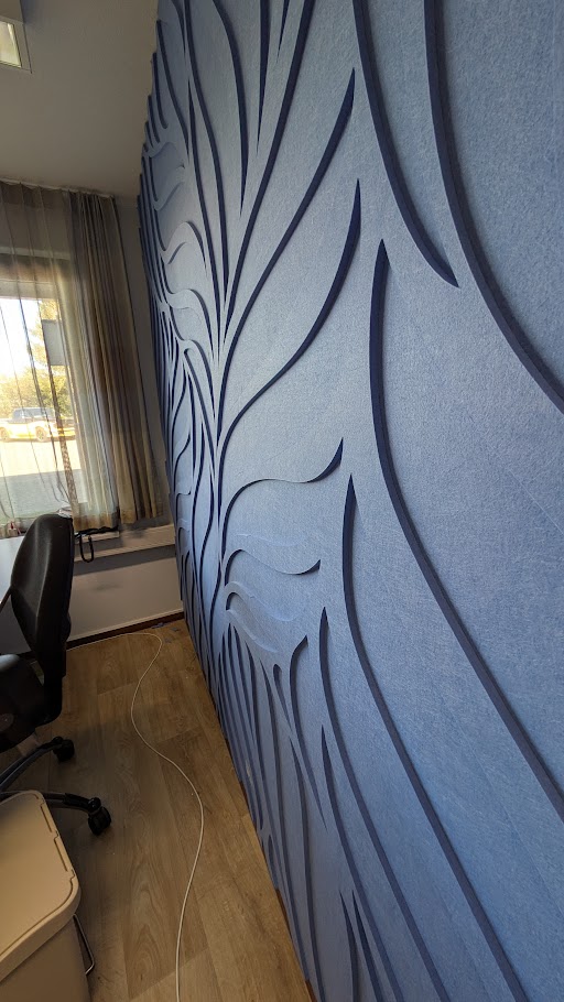 Blauwe muur met verhoogd abstract golfpatroon in een kamer met houten vloer en een bureaustoel.