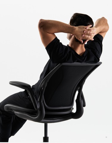 Man zit ontspannen in een ergonomische bureaustoel met zijn handen achter zijn hoofd, rug naar de camera gekeerd.
