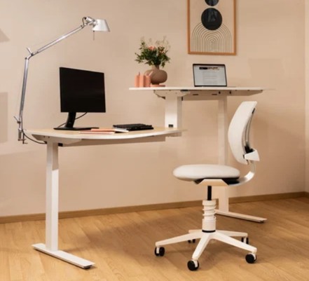 Moderne minimalistische thuiskantooropstelling met een wit verstelbaar bureau met computerscherm, toetsenbord en notitieboekje, bureaulamp en witte bureaustoel op houten vloer tegen een beige muur met ingelijste abstracte kunst en vaas met bloemen.