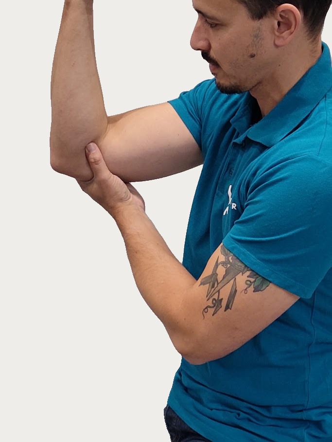 Man in blauw poloshirt masseert zijn linker elleboog met zijn rechterhand, kijkend naar de elleboog.