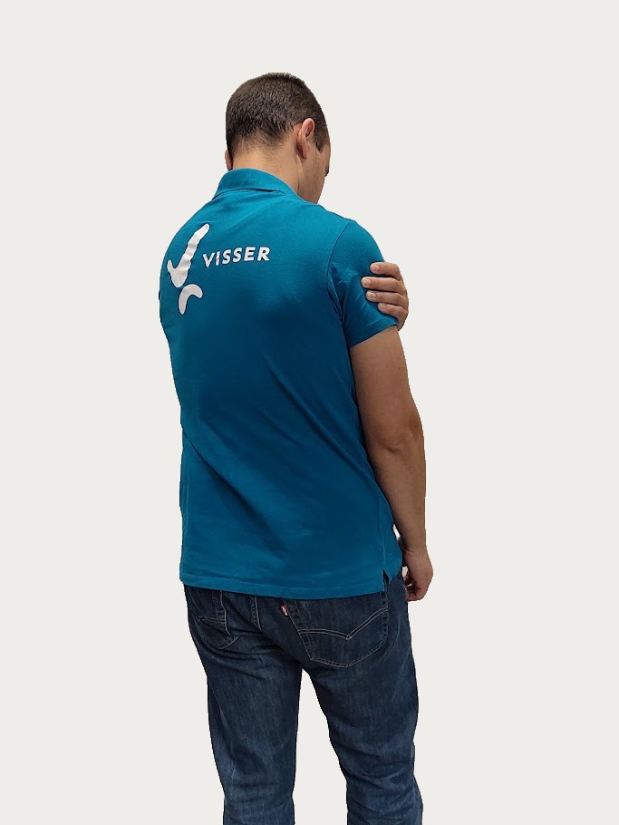 Man met donker haar, gekleed in een blauw poloshirt met het woord 'VISSER' op de rug, houdt zijn linkerschouder vast en staat tegen een effen lichte achtergrond.