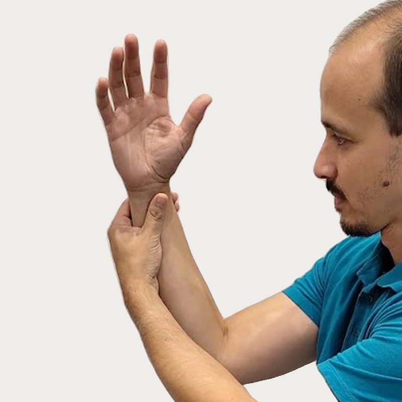 Man in a blue polo shirt holding and stretching his left wrist with his right hand against a plain light background.