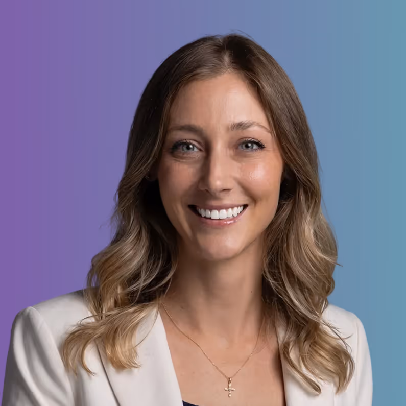 Smiling woman with long wavy hair wearing a light blazer and a cross necklace against a gradient blue-purple background.
