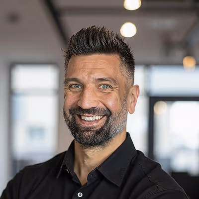 Adam, Fractional CEO, smiling man with short dark hair and beard wearing a black shirt in a bright office environment