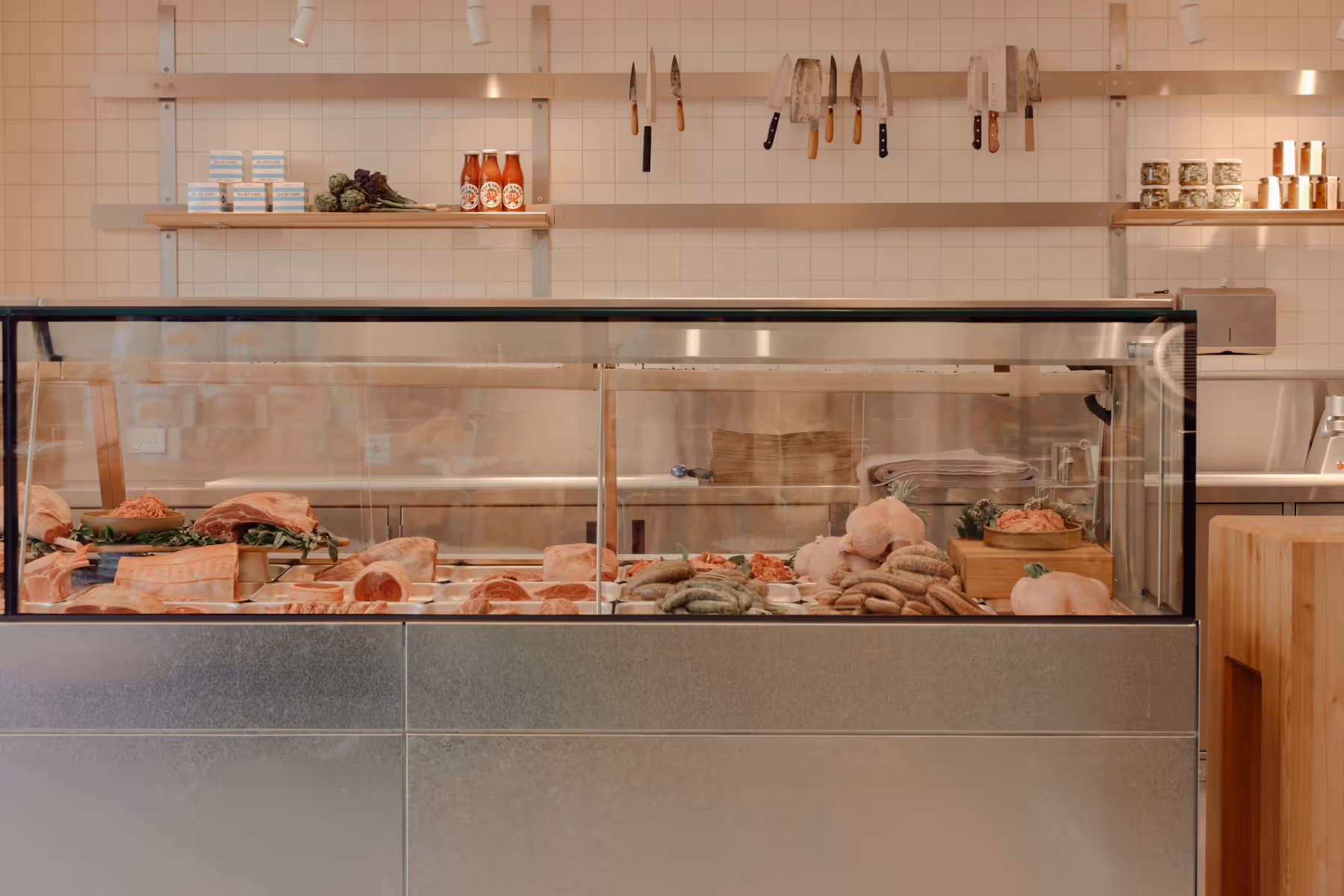 Butcher counter display case with knives on a rail above