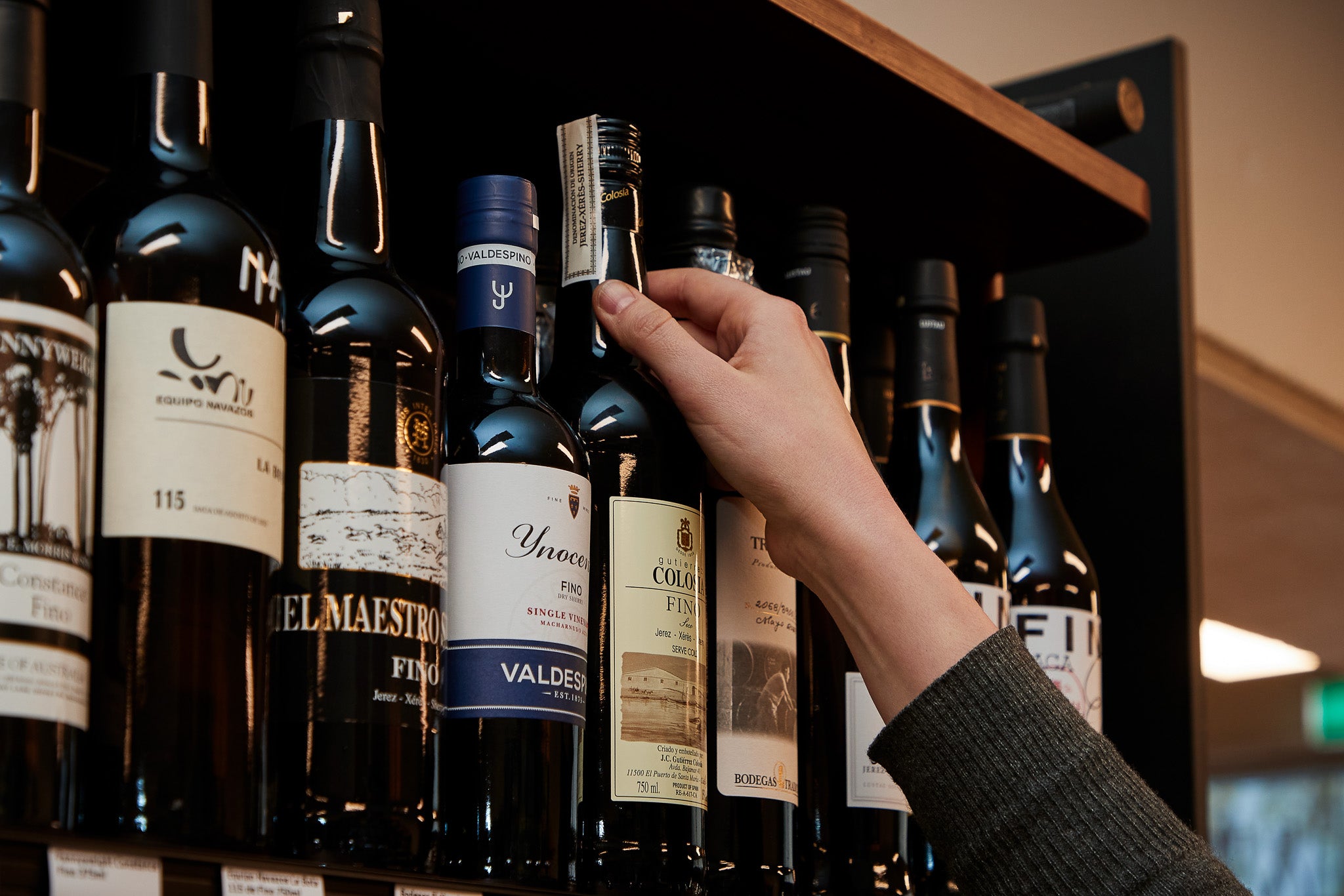 Hand taking a bottle from a wine shelf in store