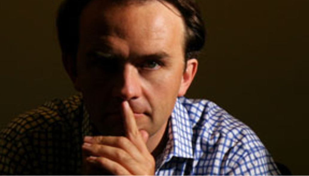 Ein nachdenklicher Mann mit einem karierten Hemd, der seine Hand nachdenklich vor dem Mund hält.