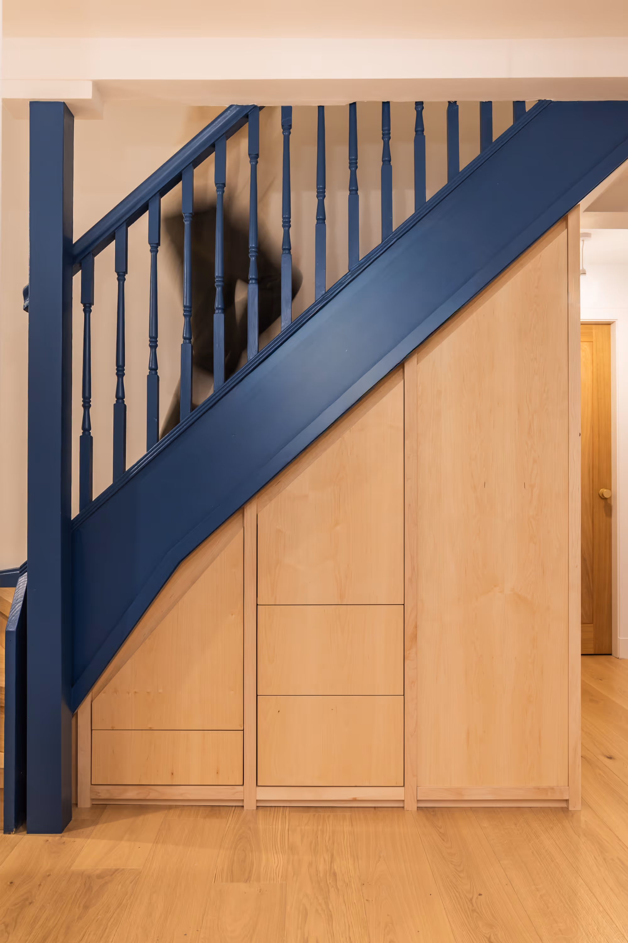 Photograph of bespoke under-stair storage with drawers closed and someone walking on the stairs