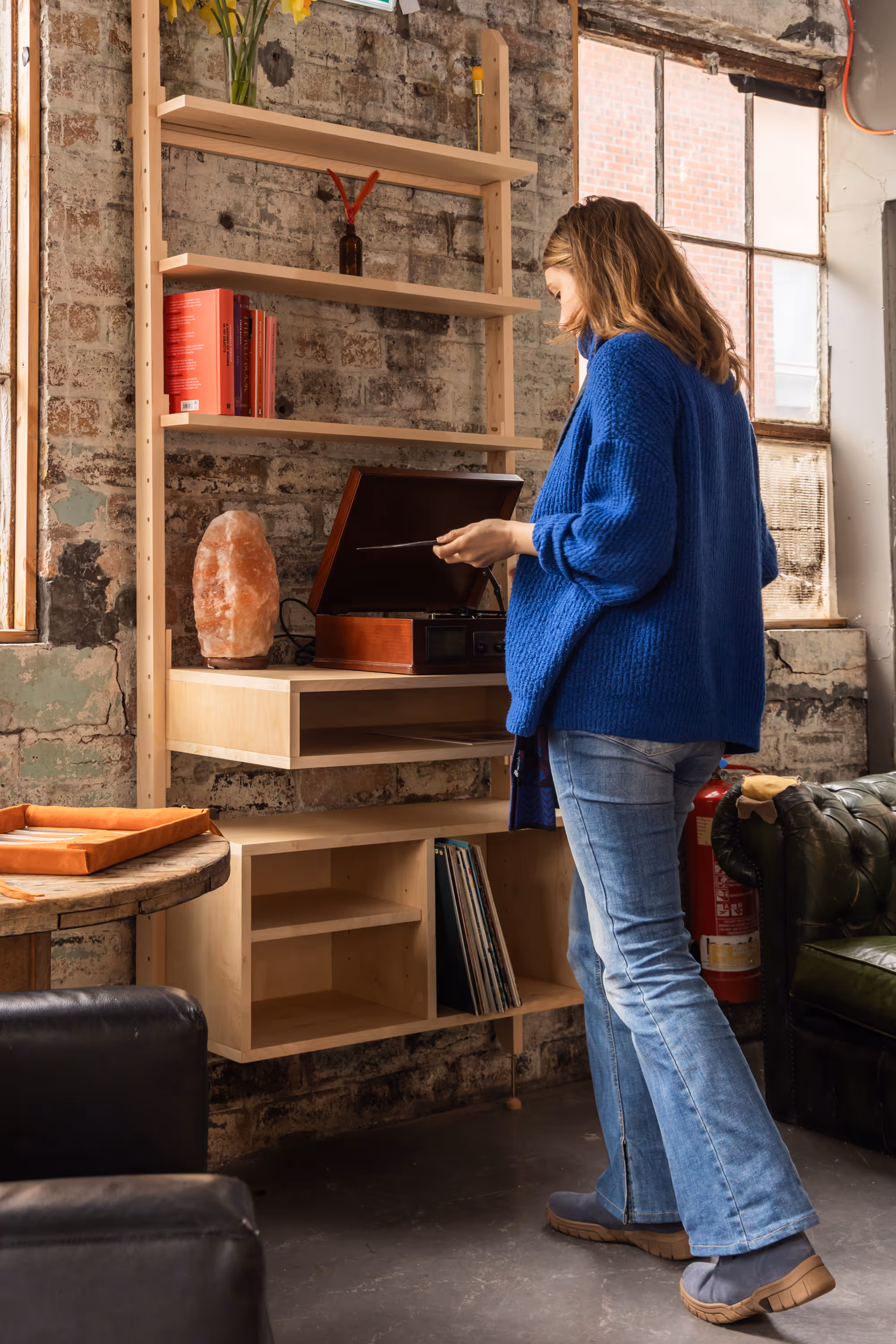 A woman standing using a record player on a custom Forma shelving unit