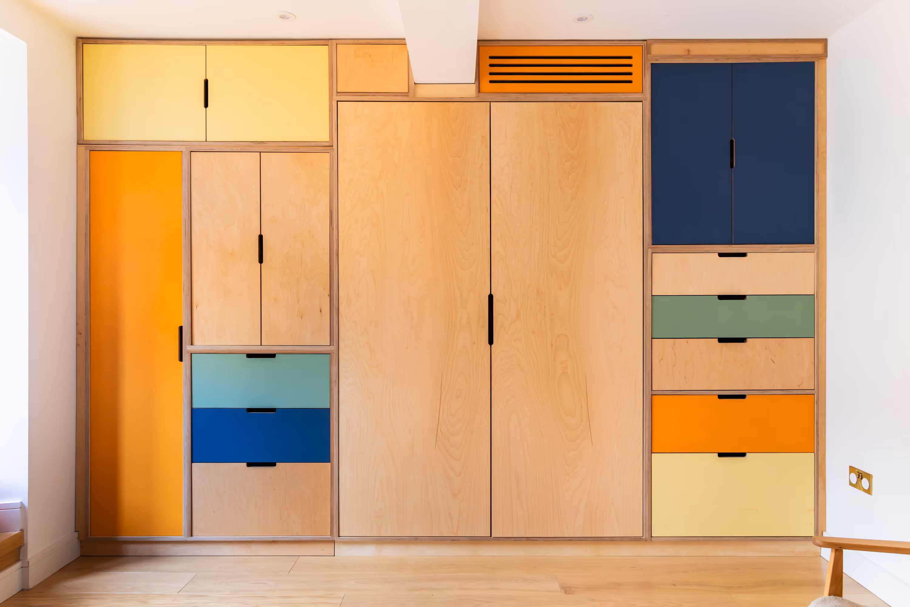 A large custom storage unit, with drawers and cabinets closed. Plywood with some painted fronts to the cabinetry