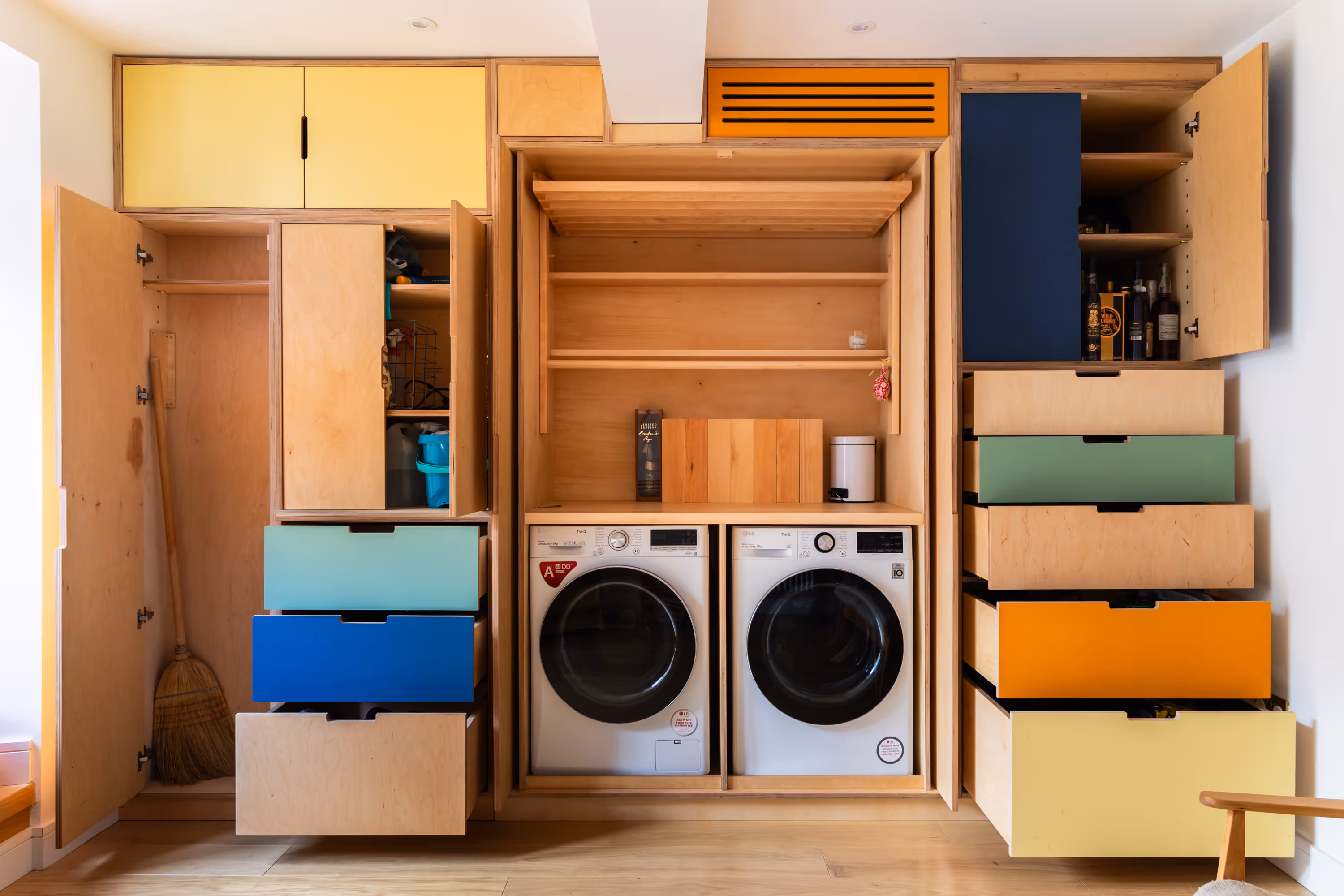 A large custom storage unit fully opened to reveal a lot of storage, include drawers and a cupboard, a drying rack and a built in washer and dryer