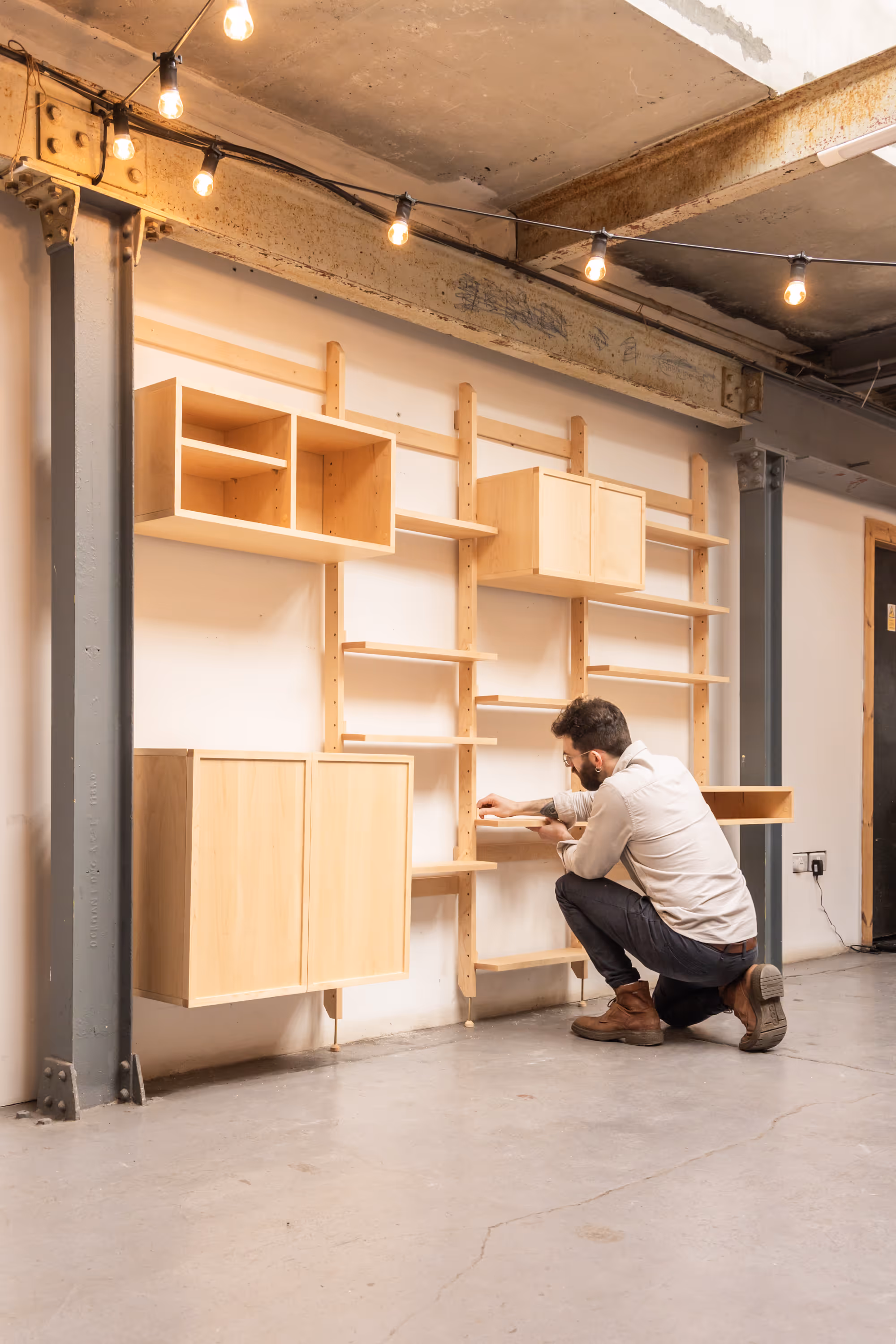 A large, four-bay Forma shelving unit by Bruntsfield Designs. A man kneeling beside it setting it up attaching an element