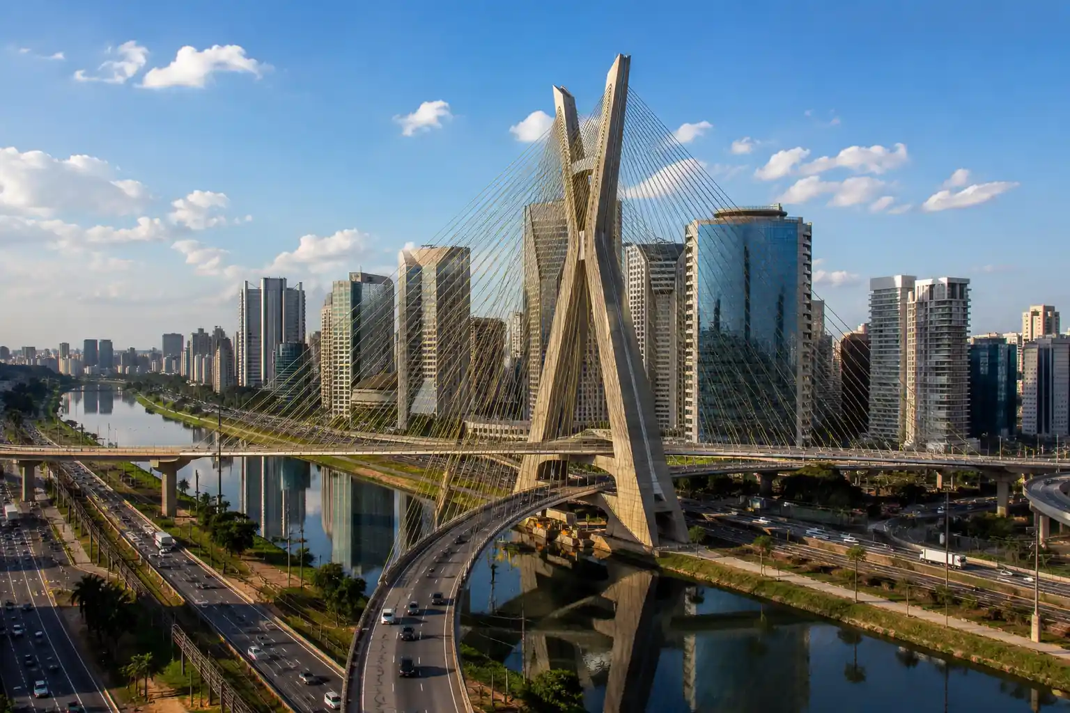 Vista aérea da Ponte Estaiada Octávio Frias de Oliveira em São Paulo, cercada por edifícios modernos, vias expressas e o centro empresarial da cidade.