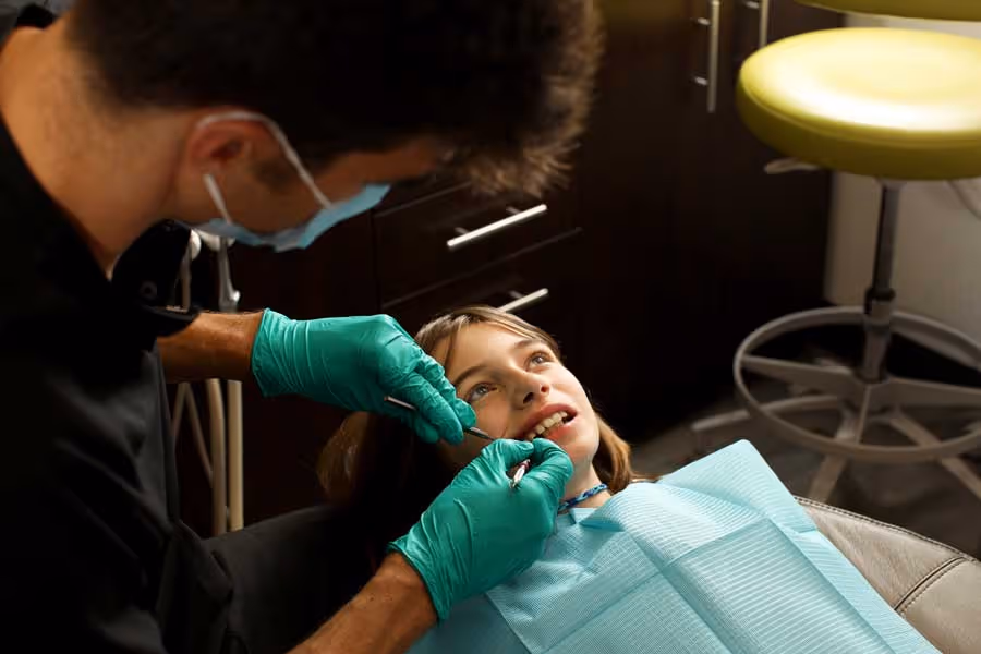 Dentist wearing gloves and mask examining a young girl's teeth in a dental clinic.