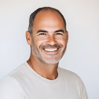 Smiling middle-aged man with short dark hair and light stubble wearing a white shirt against a light background.