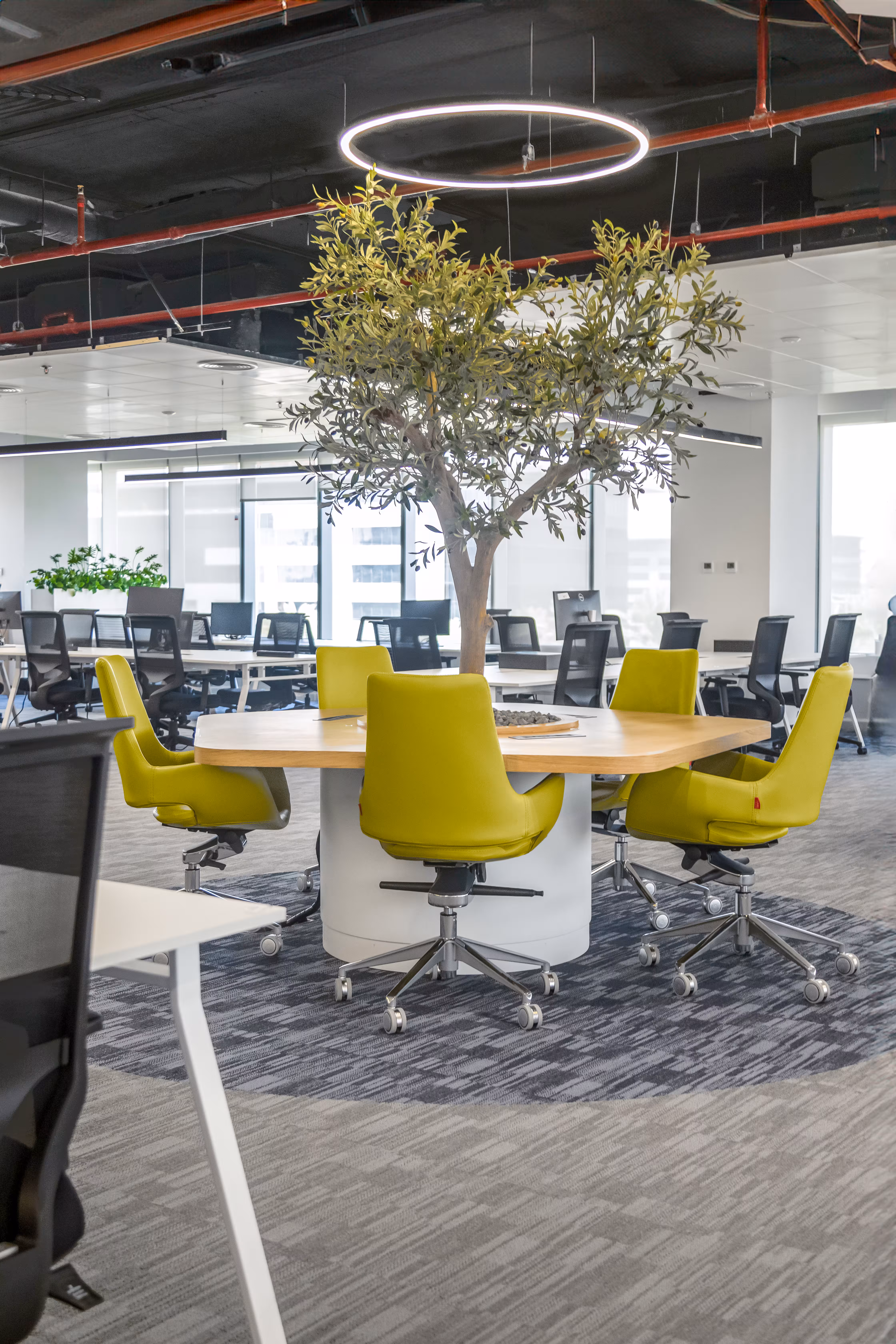 Modern office space with a white high table, brown cushioned chairs, black mesh chairs, and potted plants.