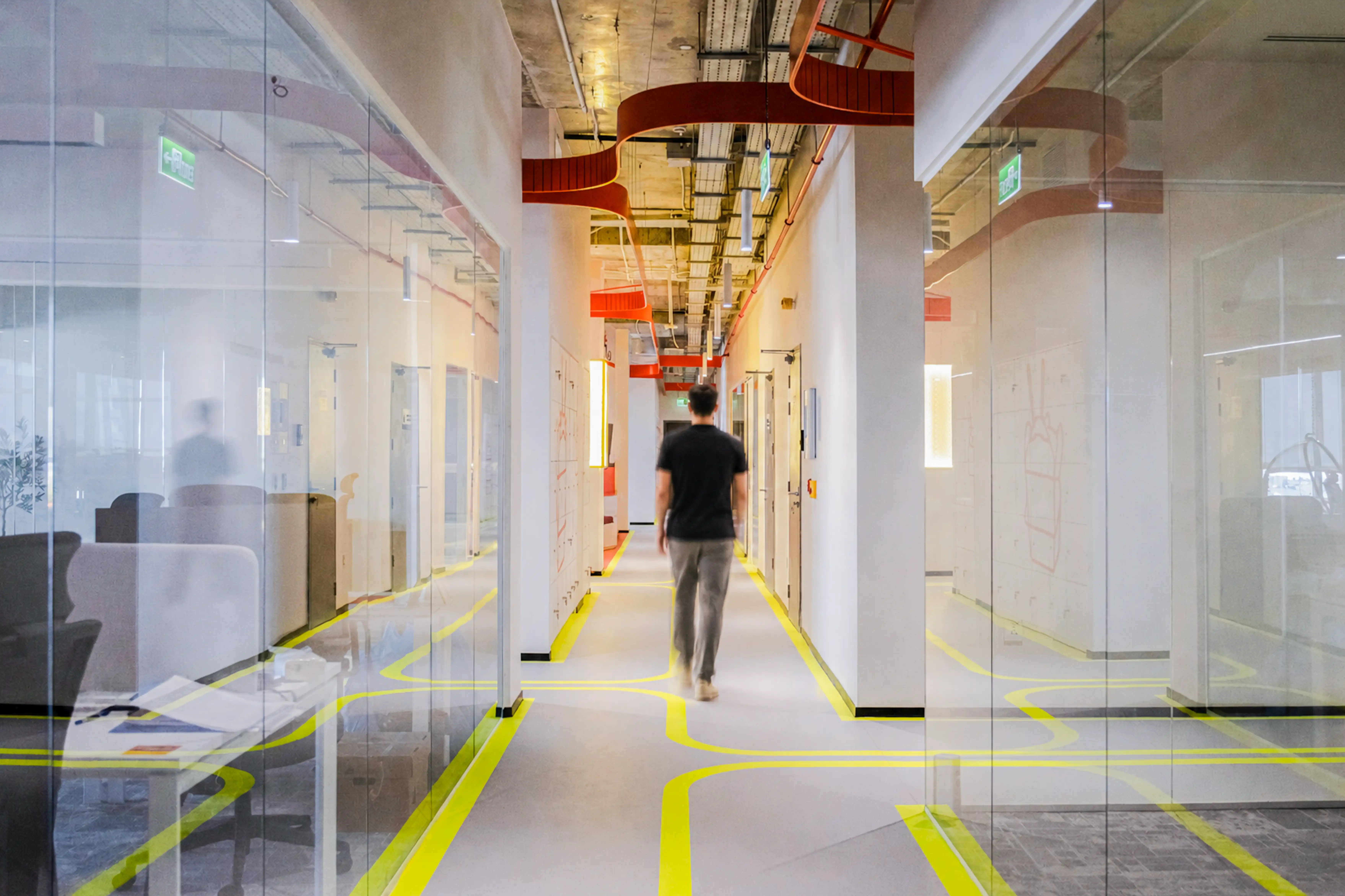 Modern office space with wooden booths featuring cushioned seating and tables, glass walls with decorative dot patterns, and a motivational quote on the wall.