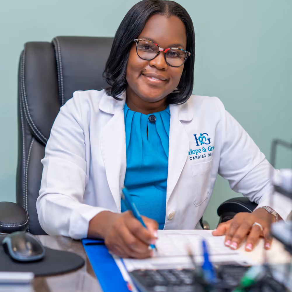 Smiling female doctor in white coat writing on clipboard at office desk.
