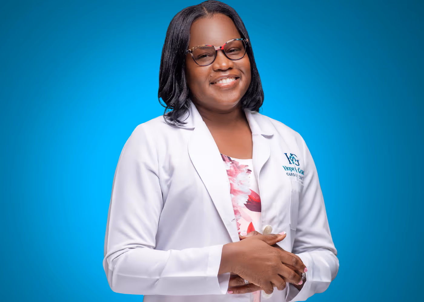 Smiling woman wearing glasses and a white medical coat against a blue background.