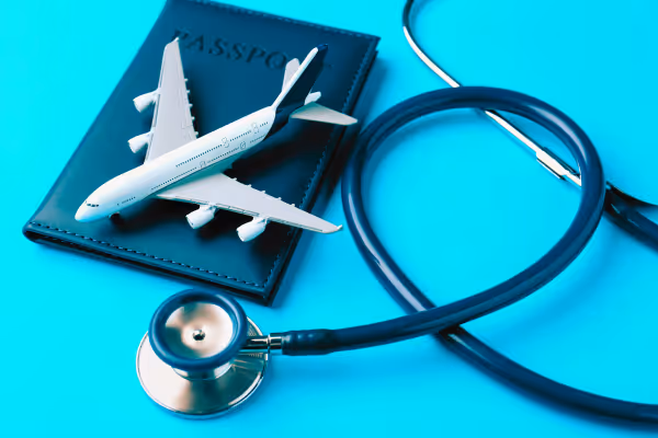 Model airplane on a passport next to a stethoscope on a blue surface, symbolizing medical tourism.