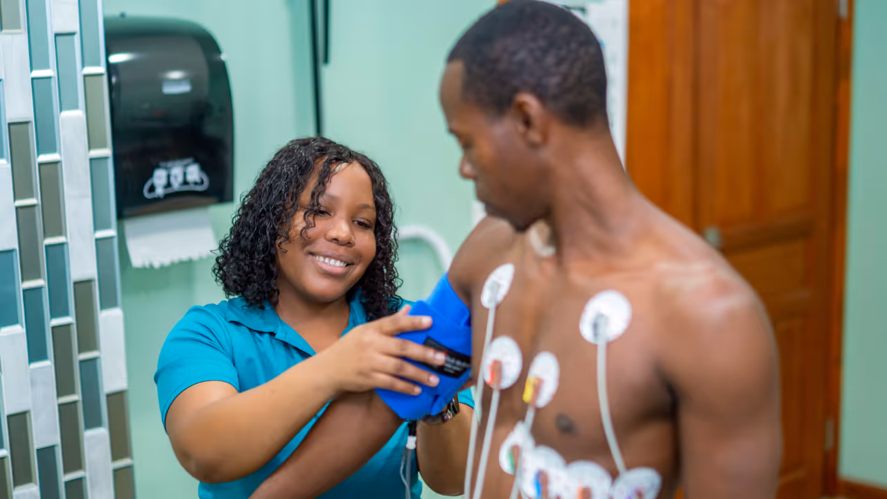 Smiling healthcare worker measures blood pressure of shirtless man with sensors on his chest.