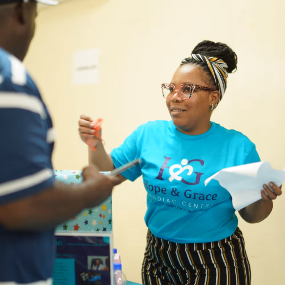 Woman in blue Hope & Grace T-shirt handing papers and a red item to a man in striped shirt.