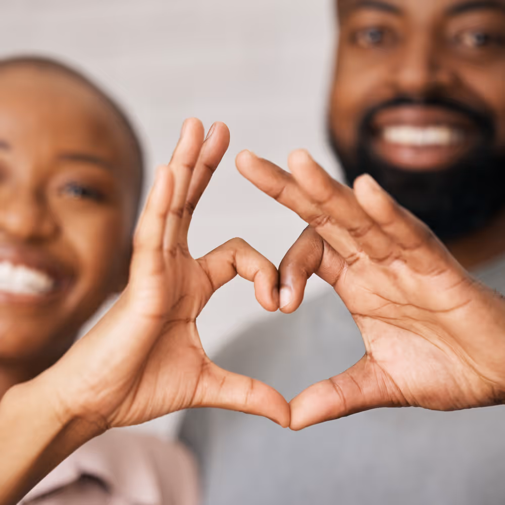 Close-up of a smiling couple forming a heart shape with their hands.
