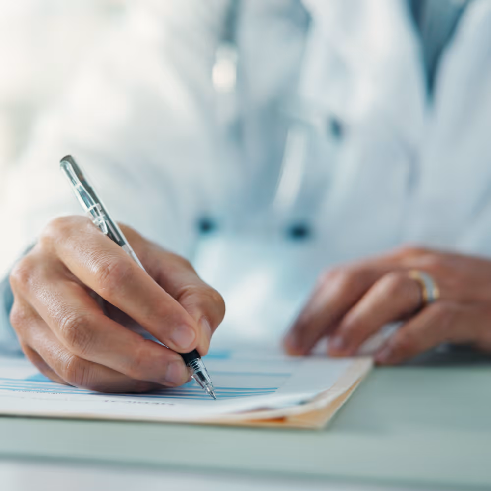 Close-up of a doctor in a white coat writing on a medical form with a pen.