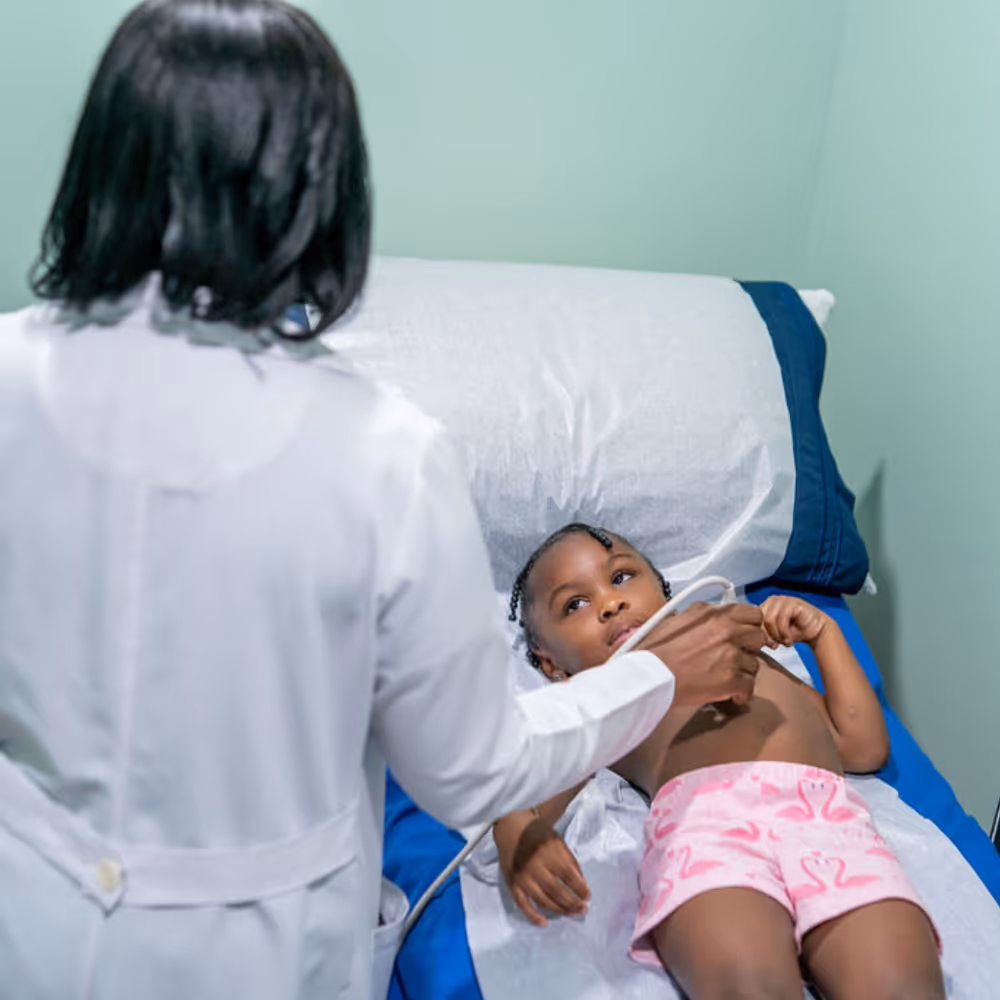 Doctor performing an echocardiogram on a young child lying on a medical bed.