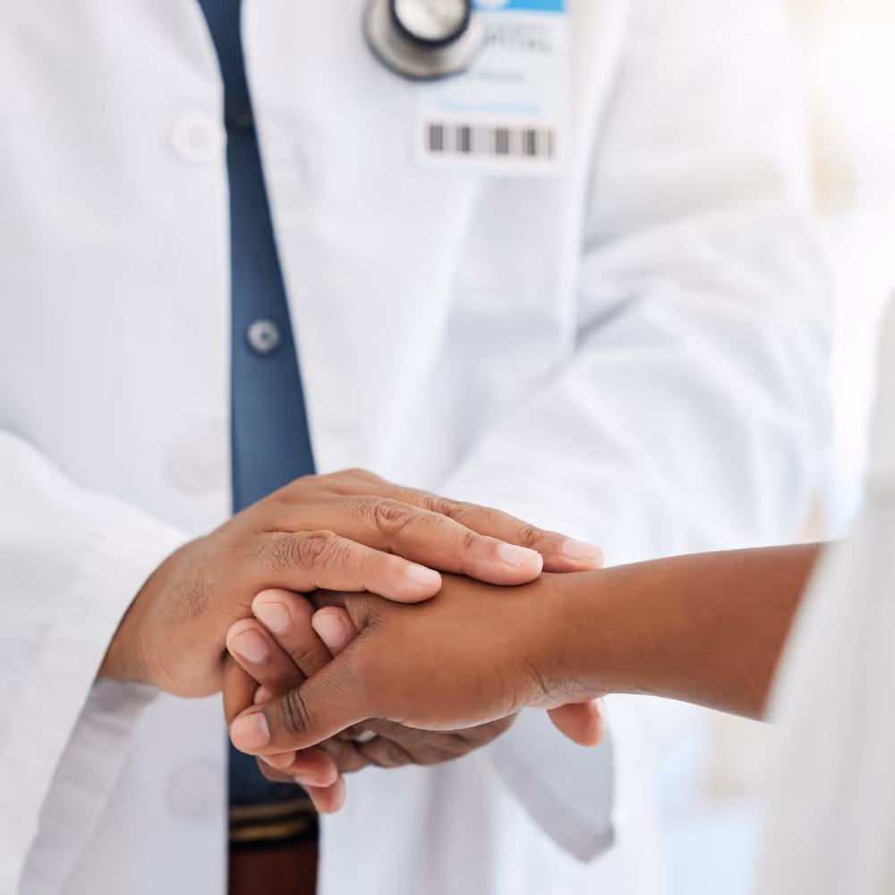 Doctor in white coat gently holding a patient's hand in a supportive gesture.