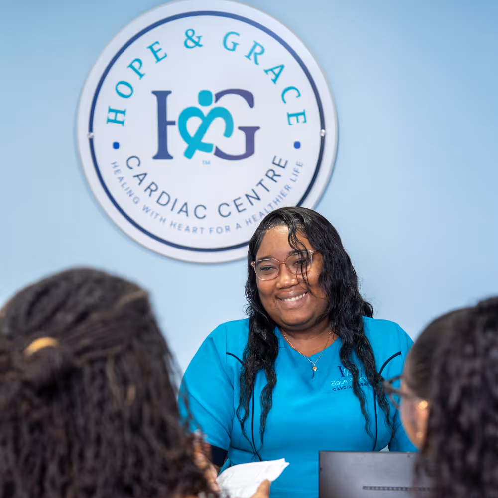 Smiling receptionist in blue uniform at Hope & Grace Cardiac Centre talking to two visitors.