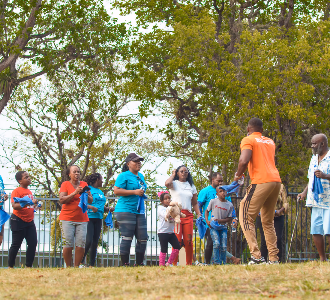 Group of people outdoors participating in a fitness or aerobics session led by an instructor in orange.