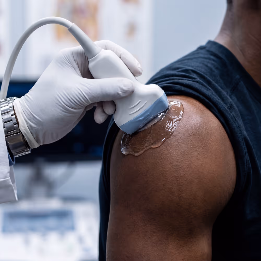 Medical professional uses ultrasound device with gel on a patient's shoulder during exam.