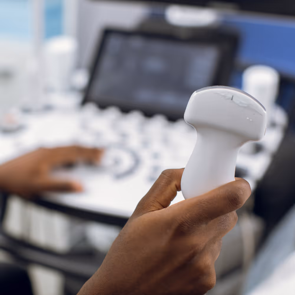 Hand holding ultrasound probe with a blurred ultrasound machine in the background.