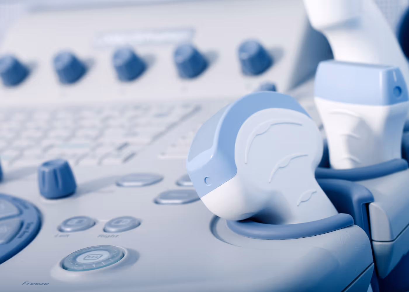 Close-up of white and blue ultrasound machine controls and probes with buttons and knobs.