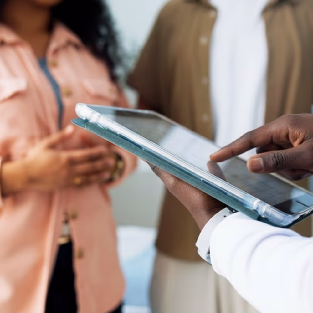 Person using a tablet to show information to two standing people in casual clothes.