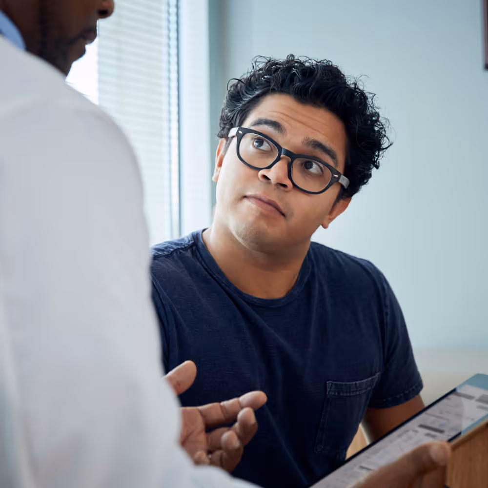 Patient with glasses attentively listening to doctor explaining details on a clipboard.