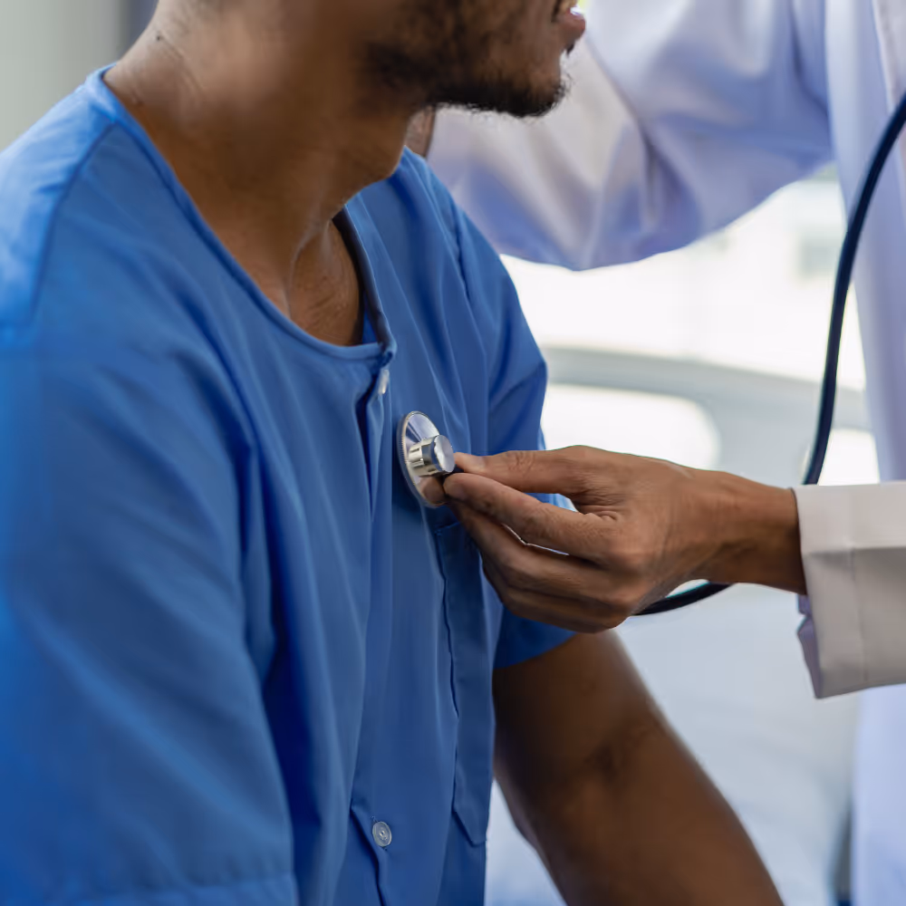 Doctor using a stethoscope to check the heartbeat of a patient wearing a blue hospital gown.
