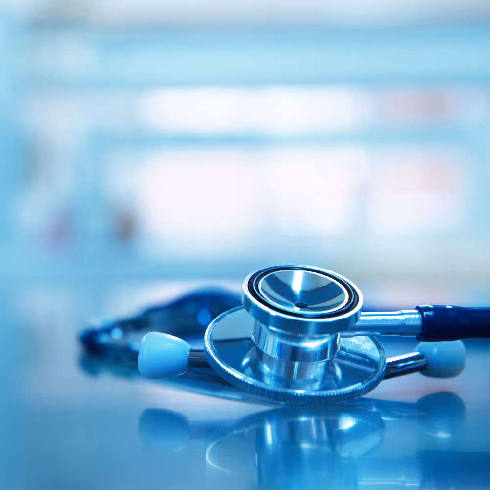 Silver and blue stethoscope lying on a reflective surface with a blurred background.