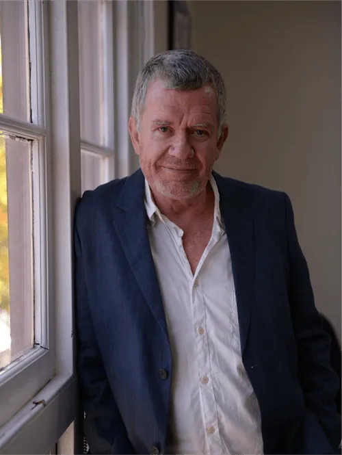Middle-aged man in navy blazer standing by window with soft light