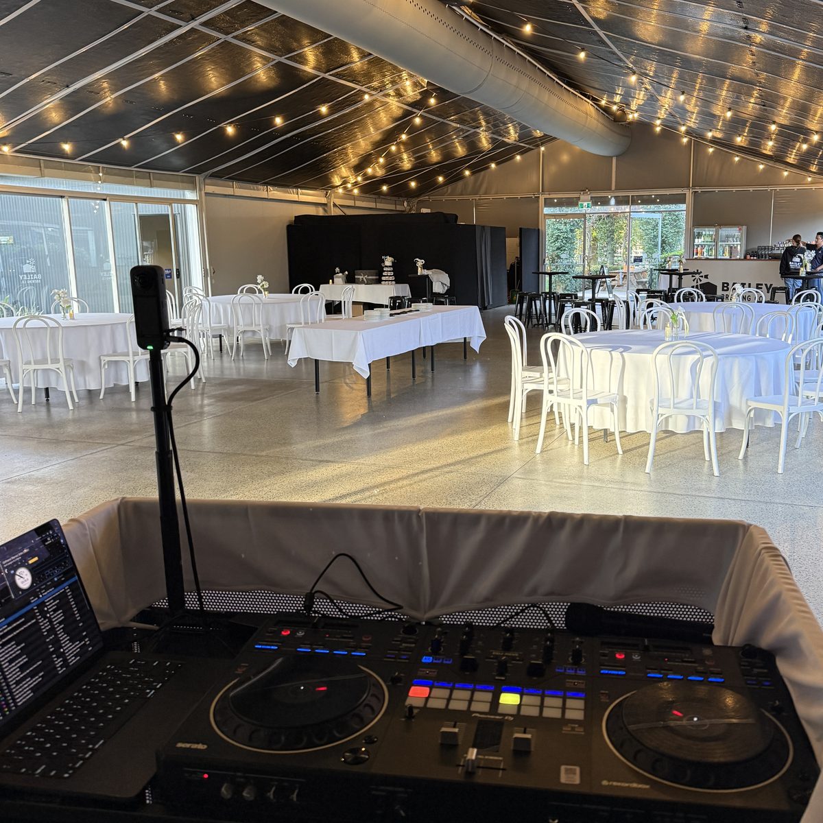 Wedding reception set up at a Perth venue seen from the DJ booth, with festoon lighting above white round tables