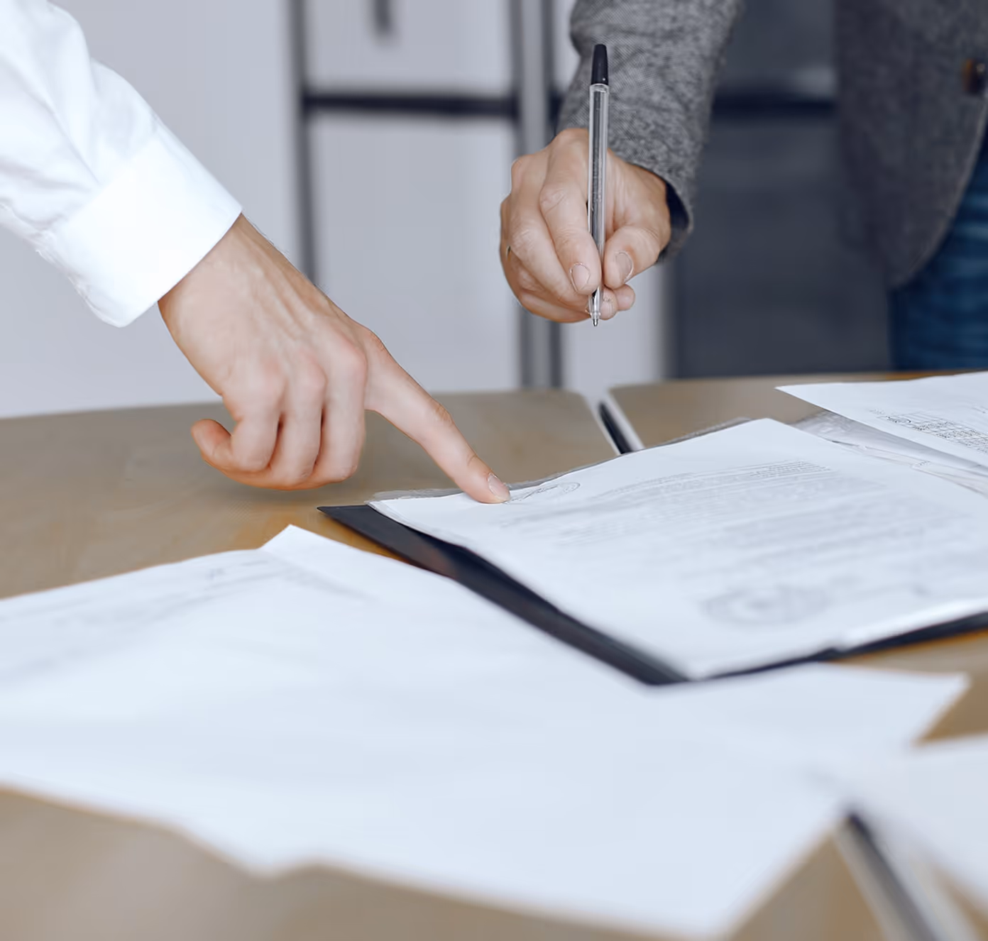 Two people reviewing and pointing to documents on a table, one holding a pen poised to write.