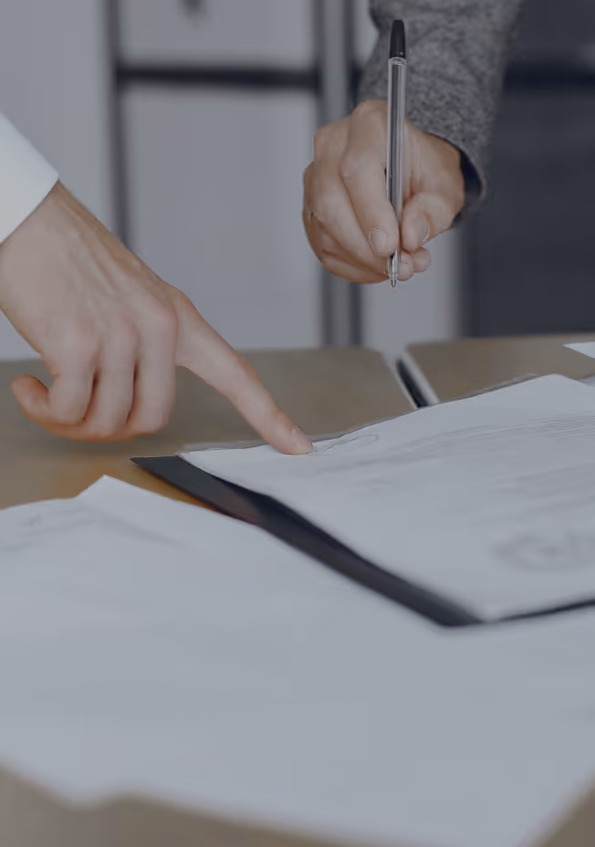 Two hands reviewing a document on a table, one pointing and the other holding a pen.