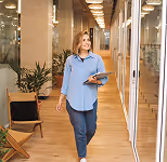 Casual woman walking in a modern office hallway holding a tablet.