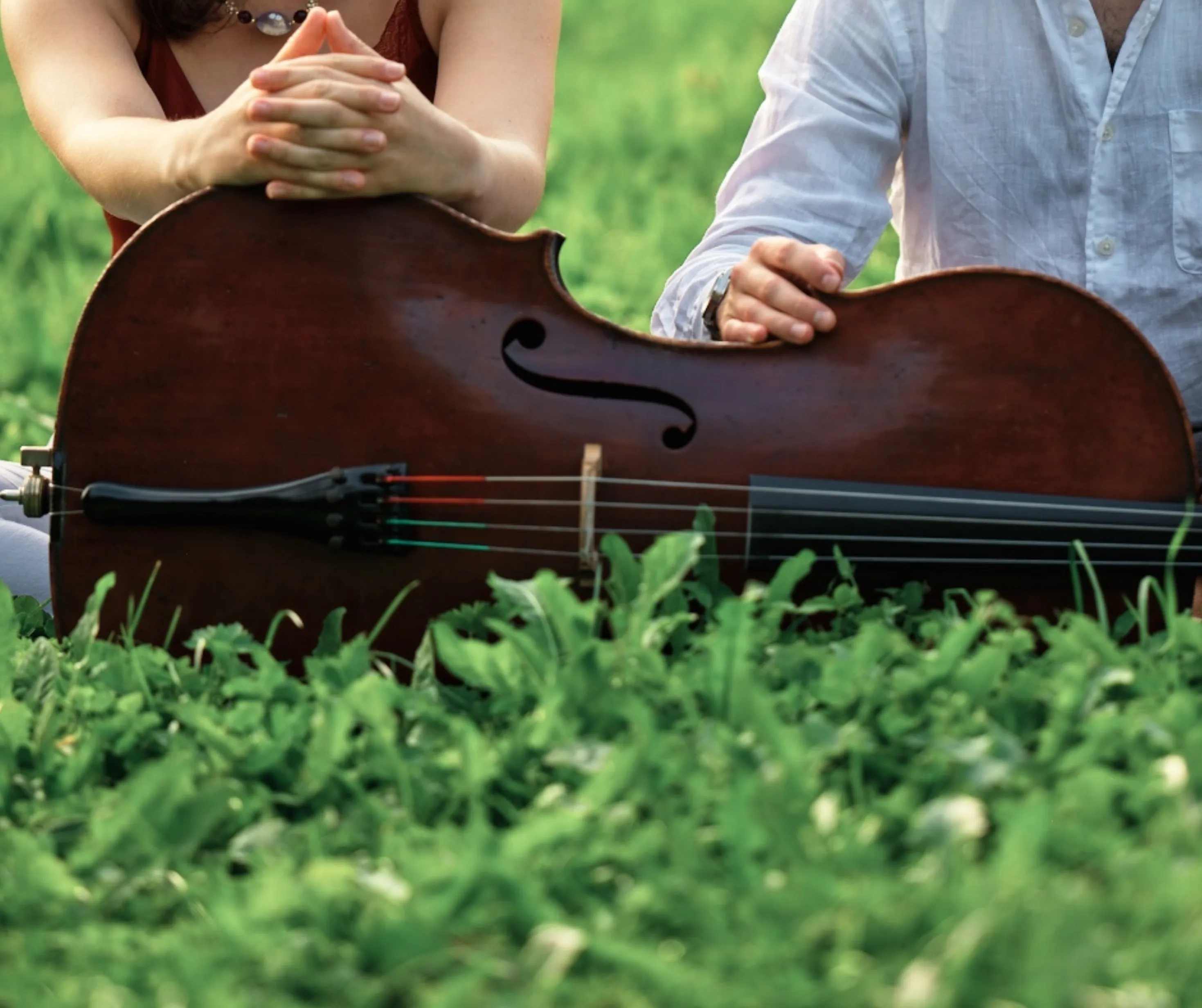 Two cellists sitting in the grass with a cello at a summer music festival
