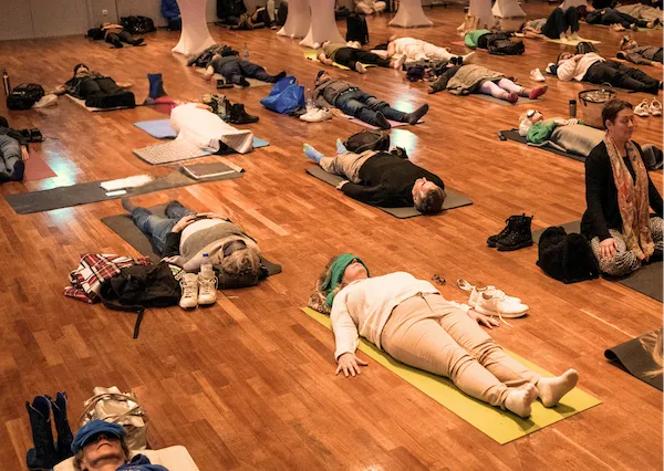 Teilnehmende liegen bei einer geführten Meditation auf Matten im Saal