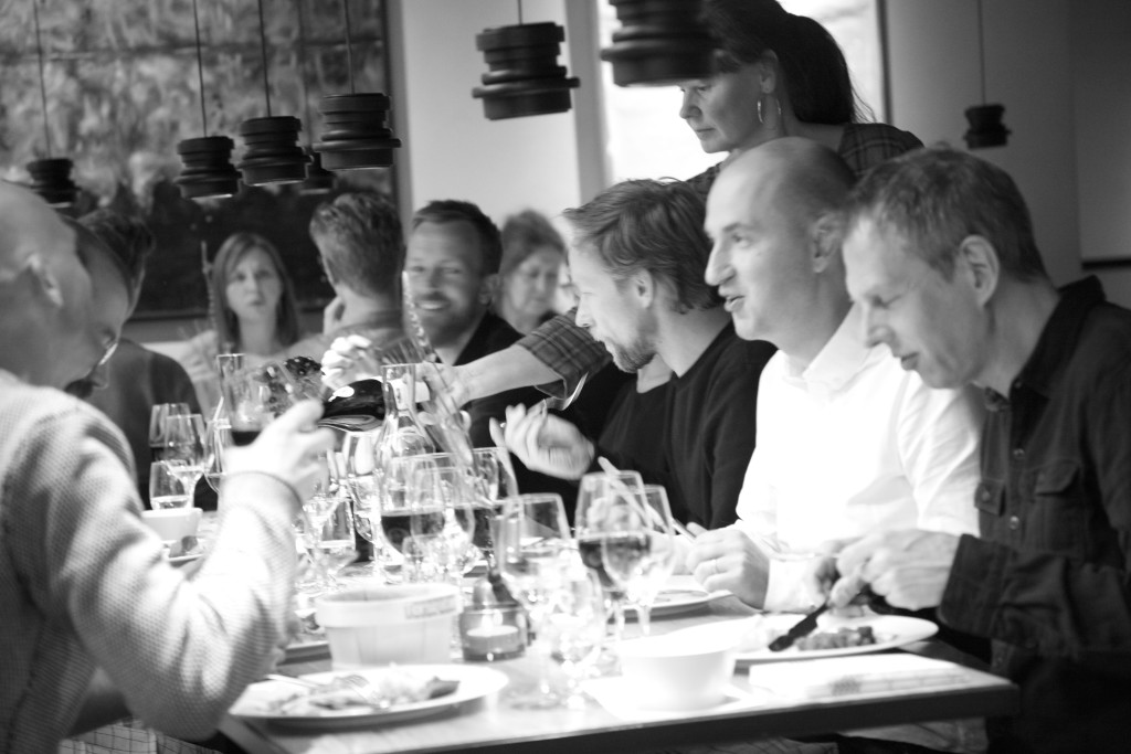 En server häller vin till gäster vid ett matbord under en samling med flera personer.