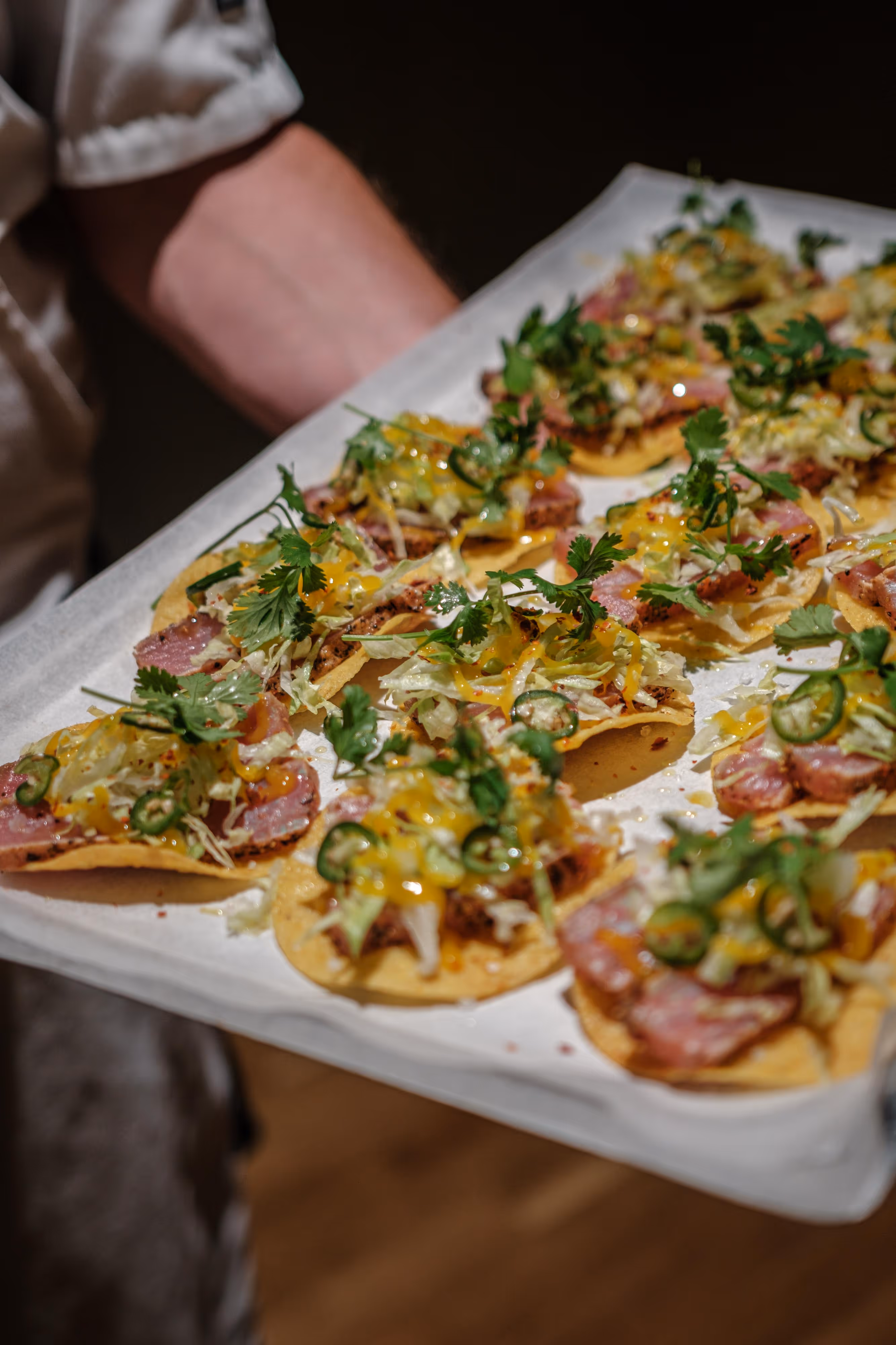Person som bär en bricka med flera tacos med skivad kött, hackad sallad, jalapeños och ost.