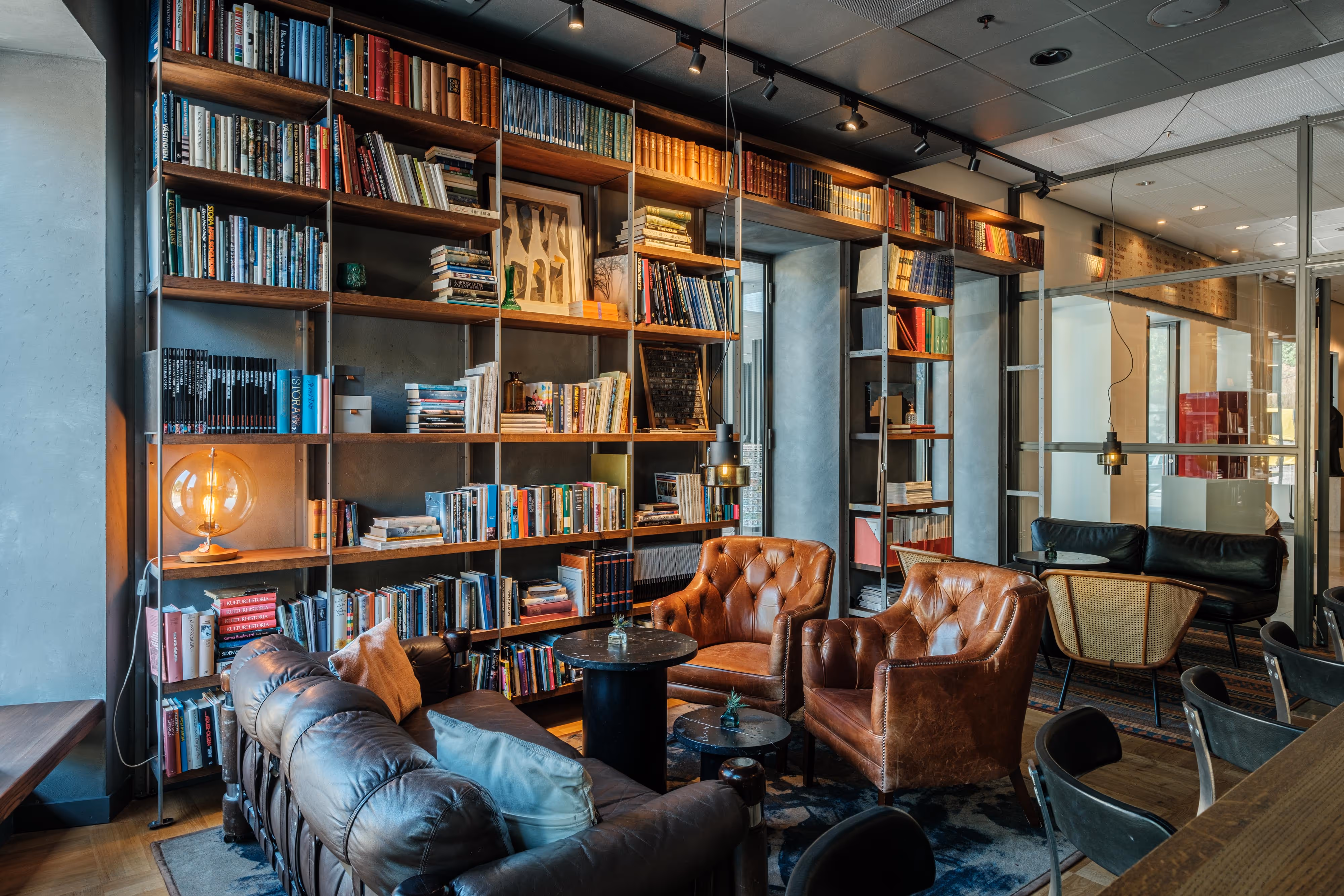 A room with a large bookshelf and brown leather chairs.